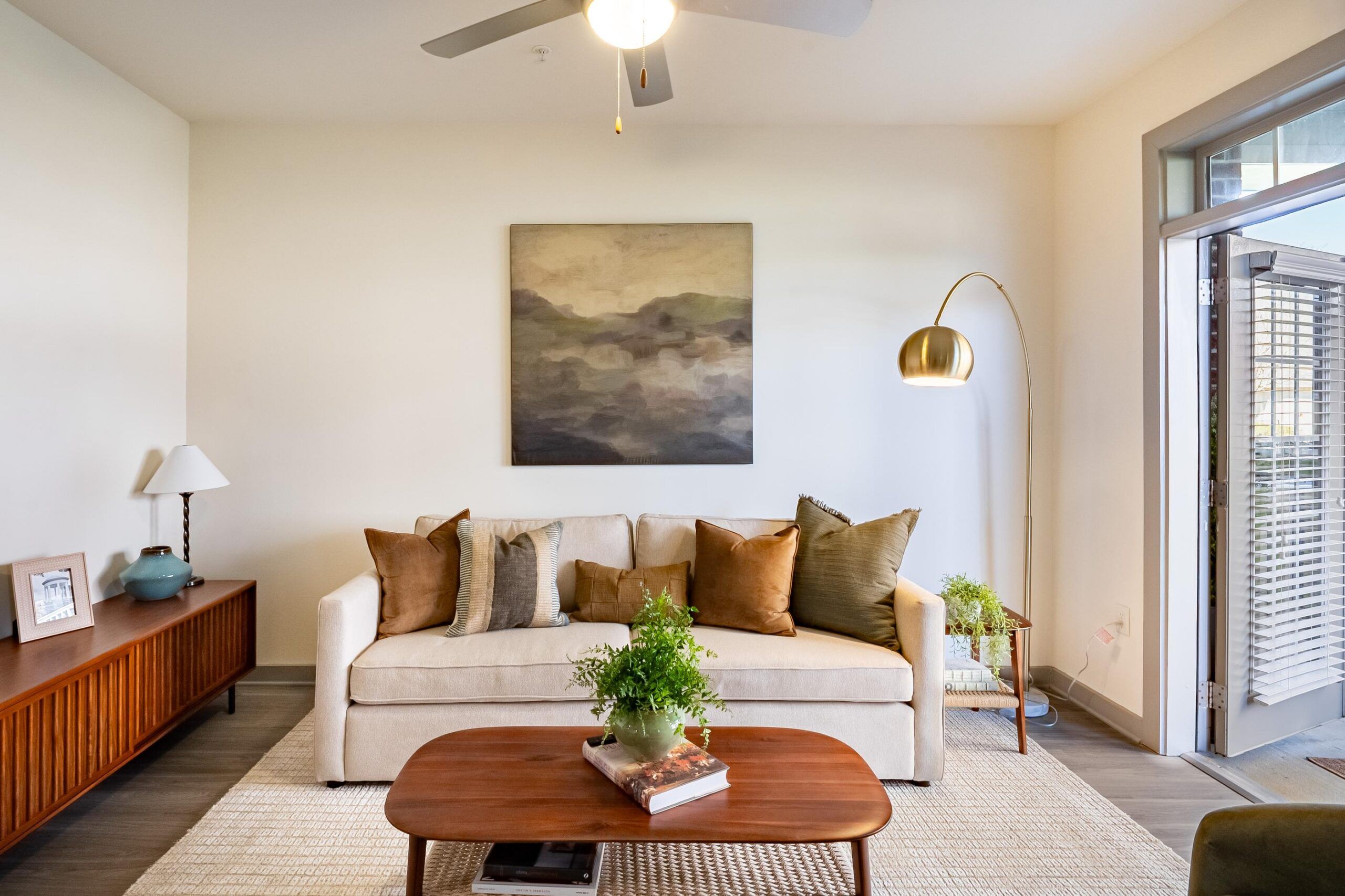 A modern living room with a beige sofa, brown pillows, wooden coffee table, and abstract wall art.