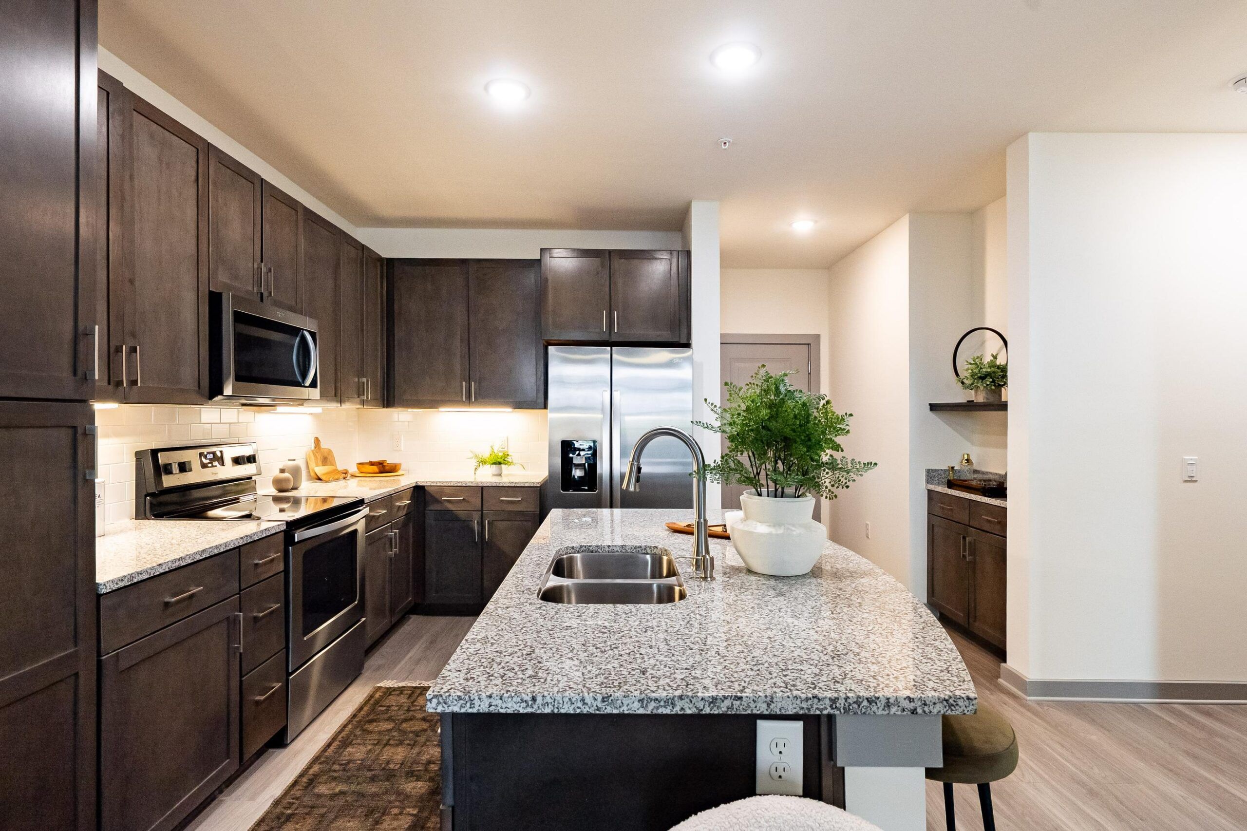 Modern kitchen with dark cabinets, stainless steel appliances, and a granite island with plants and stools.