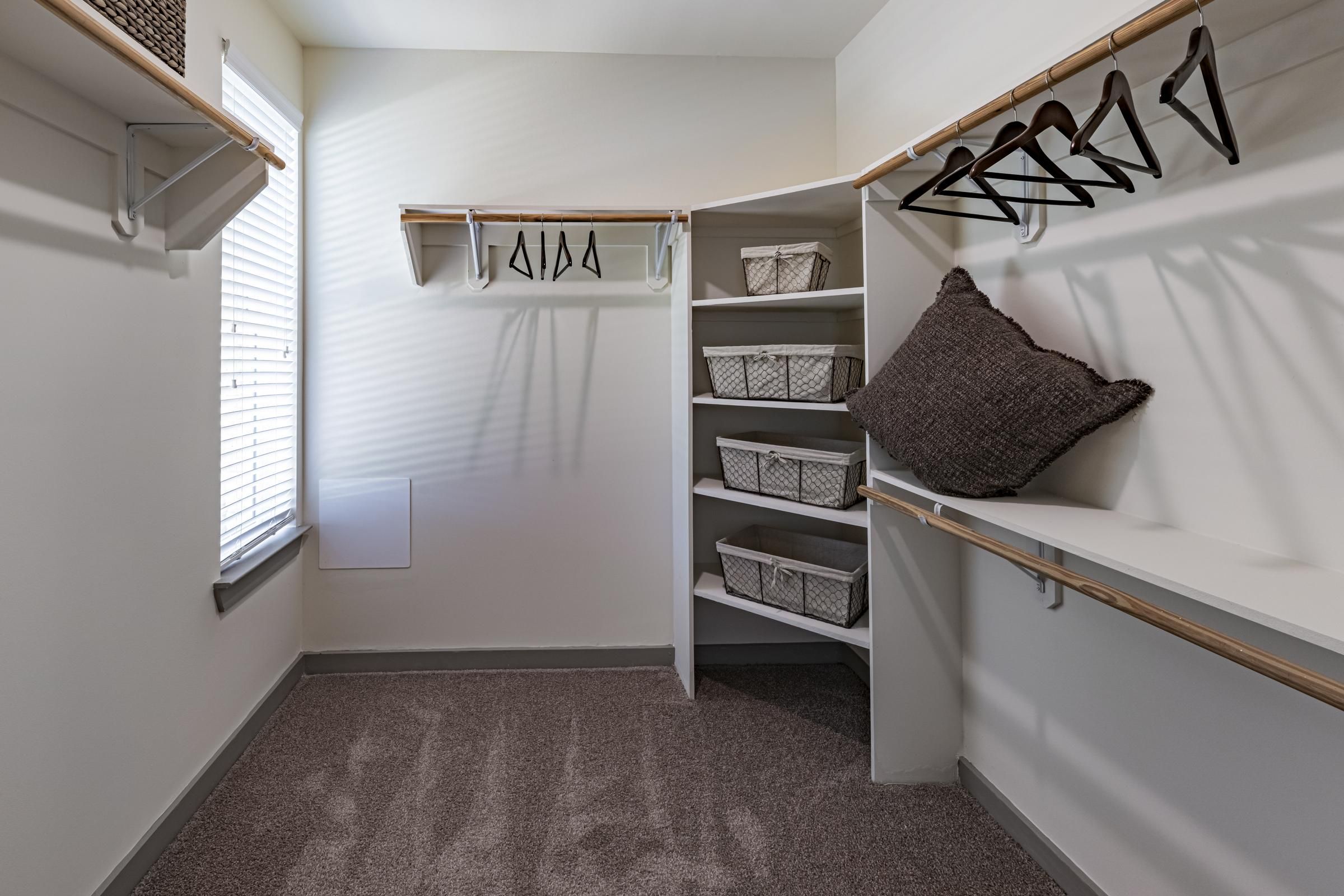Walk-in closet with shelves, baskets, empty hangers, a large pillow, and a window letting in natural light.