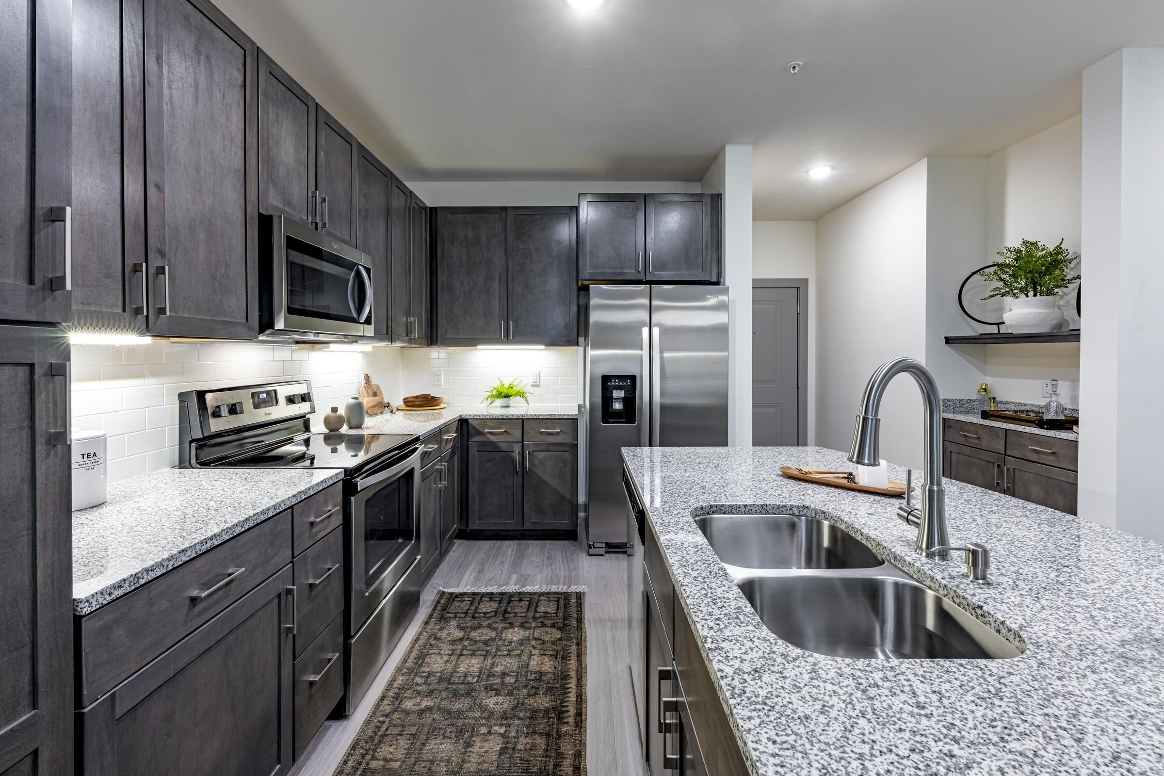 Modern kitchen with dark cabinets, granite countertops, stainless steel appliances, and a double sink island.