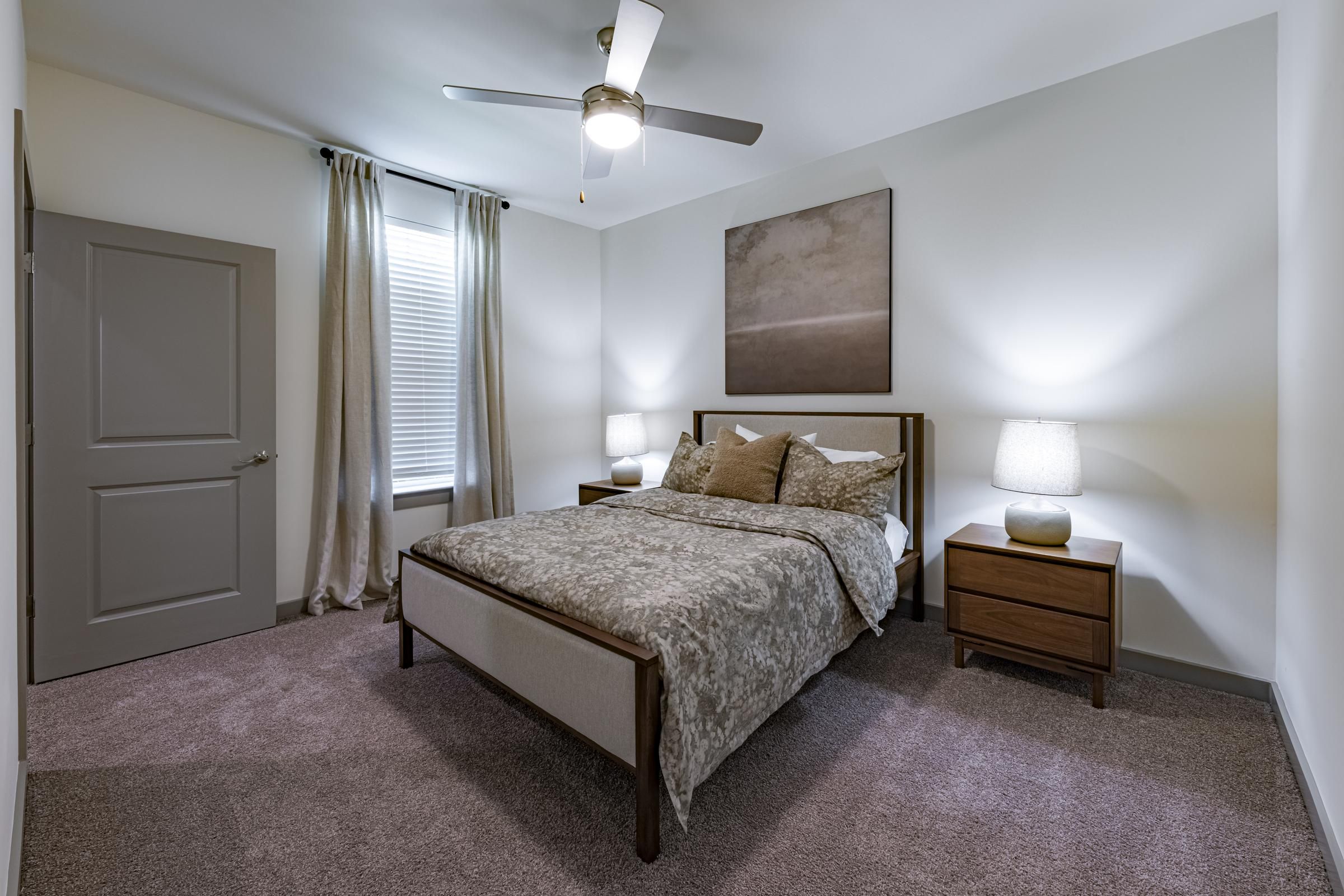 Modern bedroom with a double bed, two nightstands, lamps, a window with curtains, and a ceiling fan.
